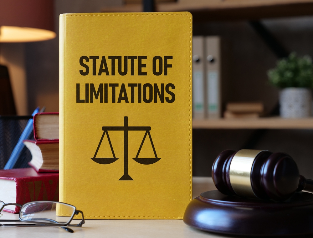Yellow book labeled “Statute of Limitations” beside a gavel and eyeglasses on a desk in a law office.