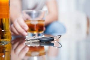 Car keys rest on the table as their owner drinks a glass of whiskey