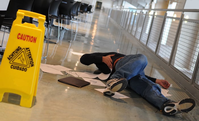 A man who slipped on a wet floor beside a bright yellow caution sign holds his back in pain