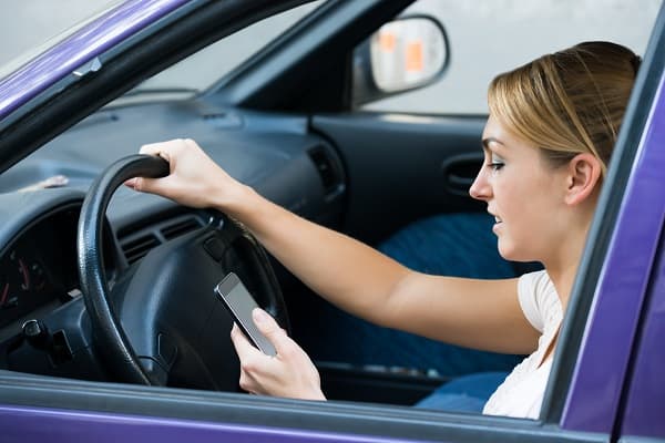 Young woman using cell phone while driving car