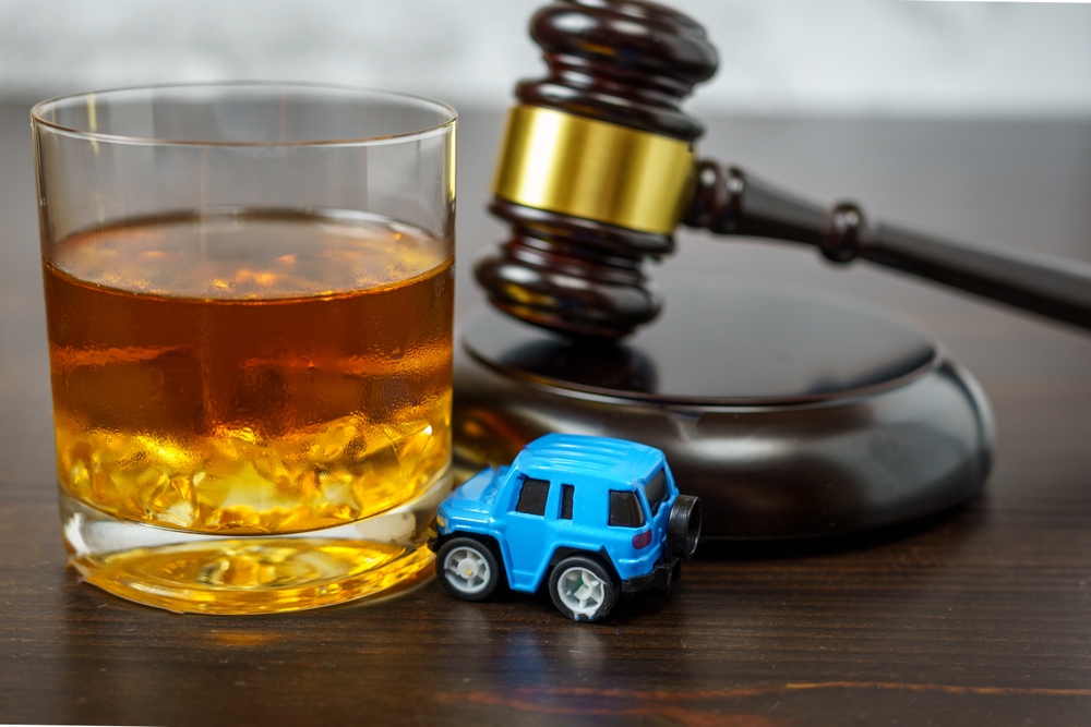 Glass of alcohol next to a judge’s gavel and toy car, symbolizing drunk driving accidents and dram shop liability cases