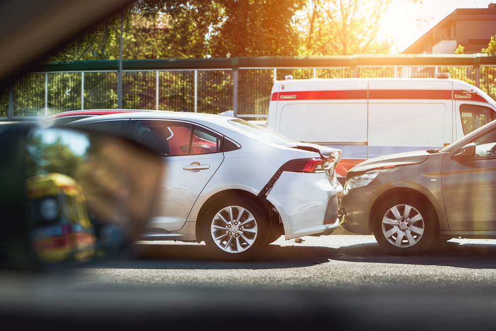Two cars involved in a rear-end collision on a city street with an ambulance in the background.