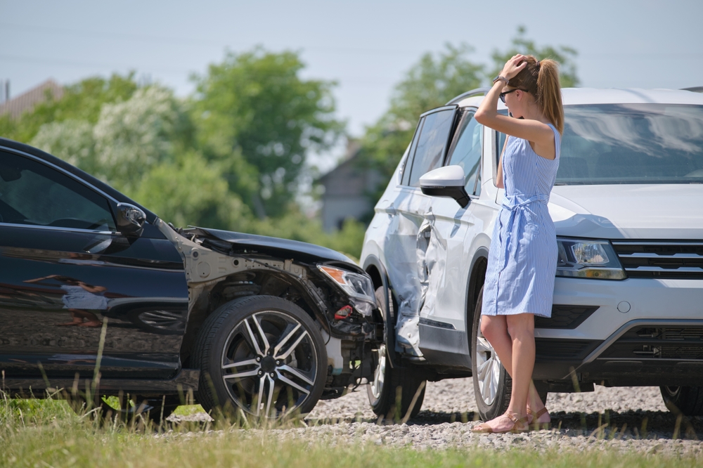 Woman standing beside two damaged cars after an accident, preparing to report the crash to police.