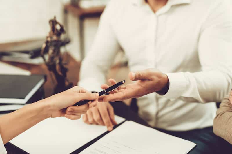 two people exchanging a pen and signing documents