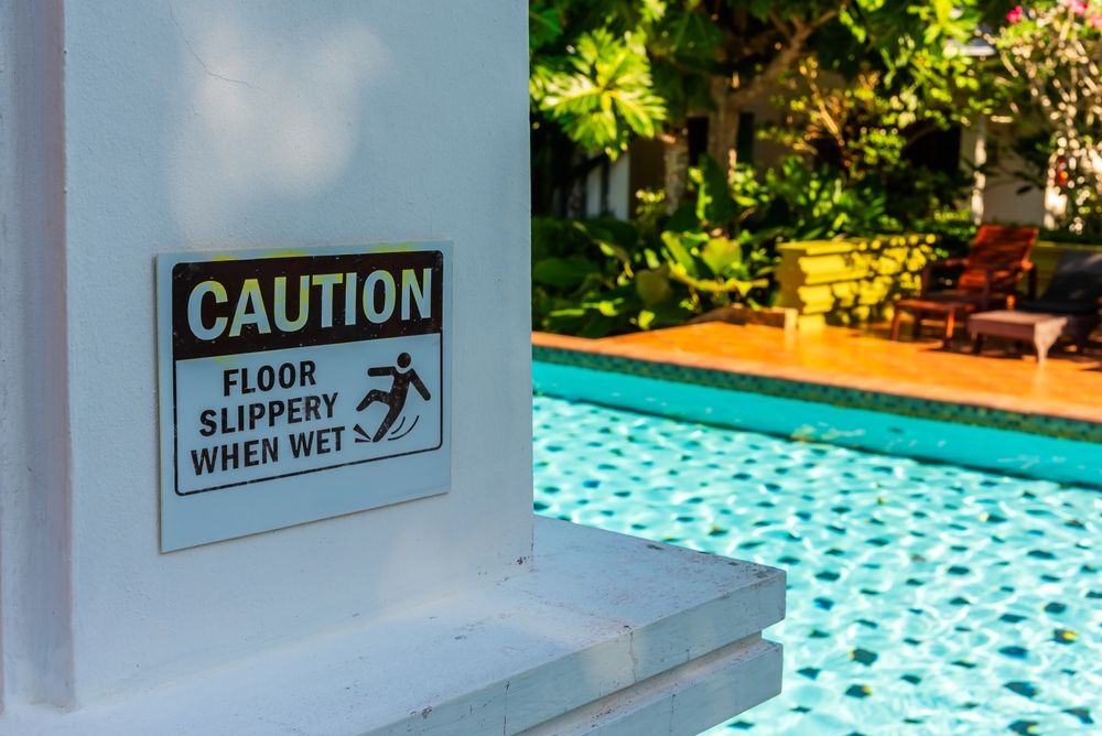 Caution sign warning about slippery floors near a swimming pool, emphasizing pool safety and property owner responsibility.