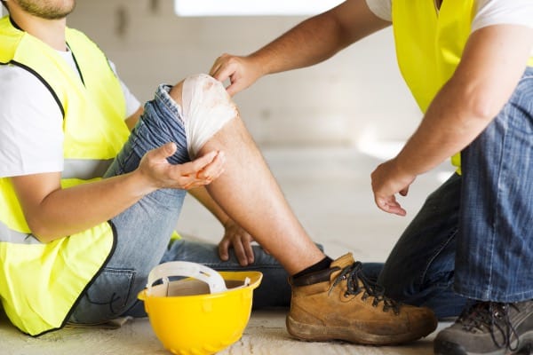 A construction worker is getting his knee bandaged after an accident.