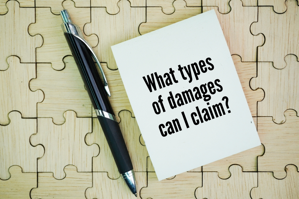 A pen and notepad on a wooden puzzle background with the text “What types of damages can I claim?”, representing compensation in a wrongful death case.