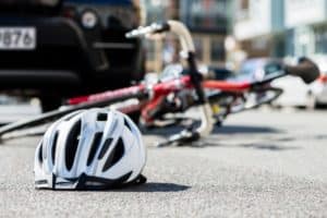 A helmet and a bike on its side are in the middle of the road are in front of a car.