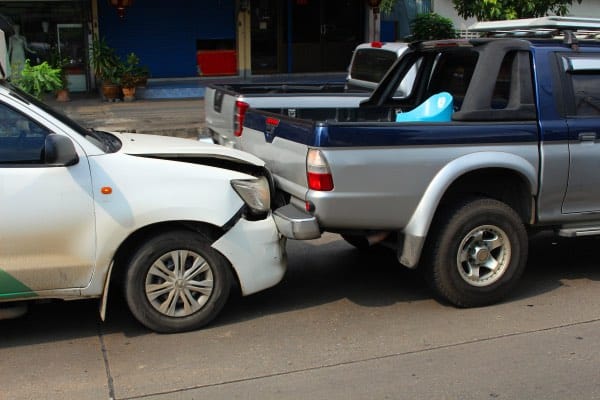 A car rear-ends a truck in the middle of a busy street.
