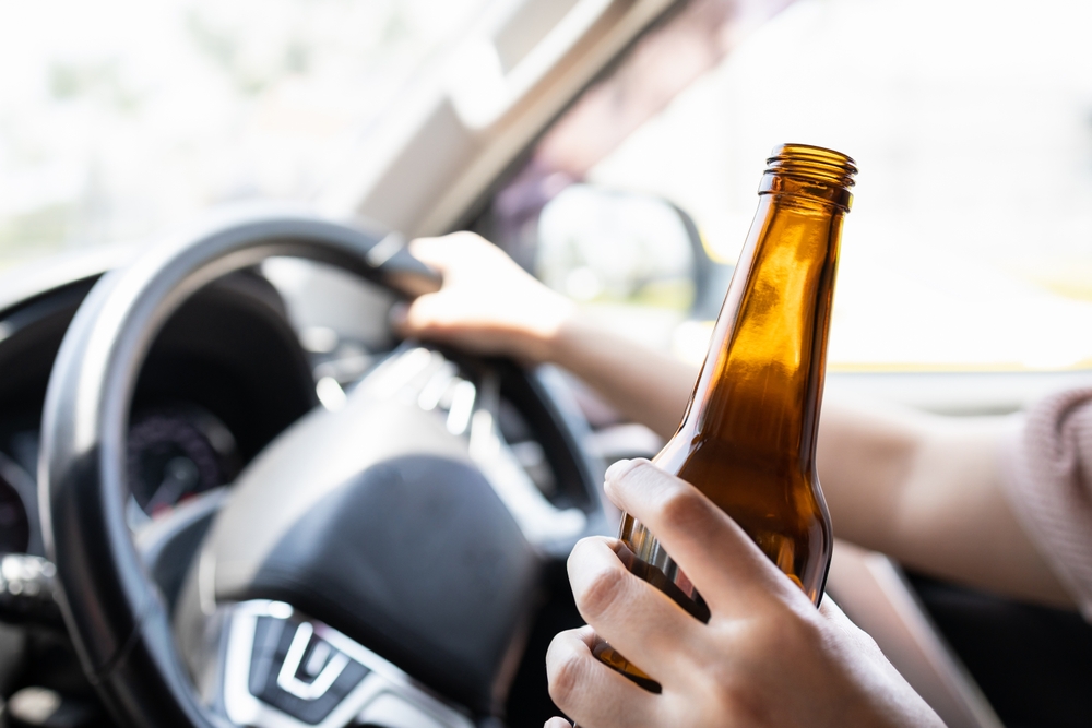 Driver holding a beer bottle while operating a vehicle, illustrating drunk driving as a major factor in DFW car accident statistics