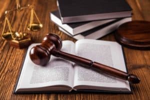 A gavel onto of a law book with a set of legal scales on a desk.