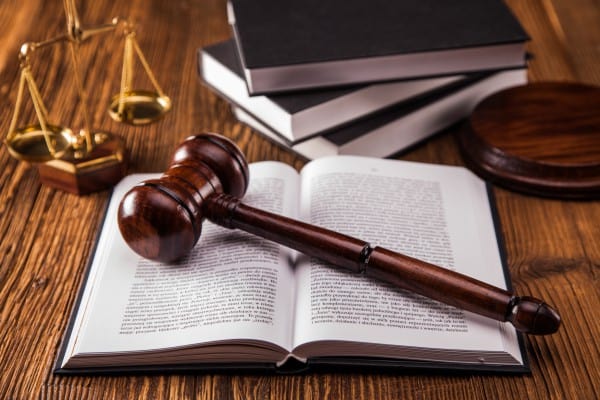 A gavel onto of a law book with a set of legal scales on a desk.