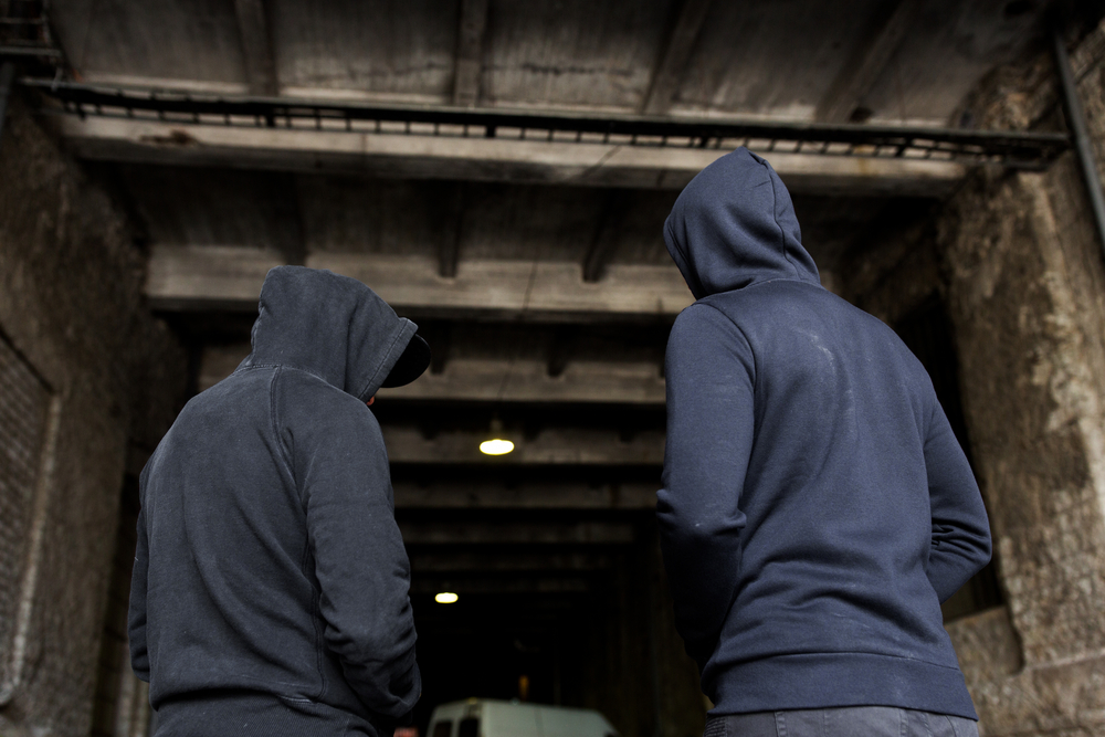 Two people in hooded clothing standing in a dark industrial area, symbolizing workplace security risks.
