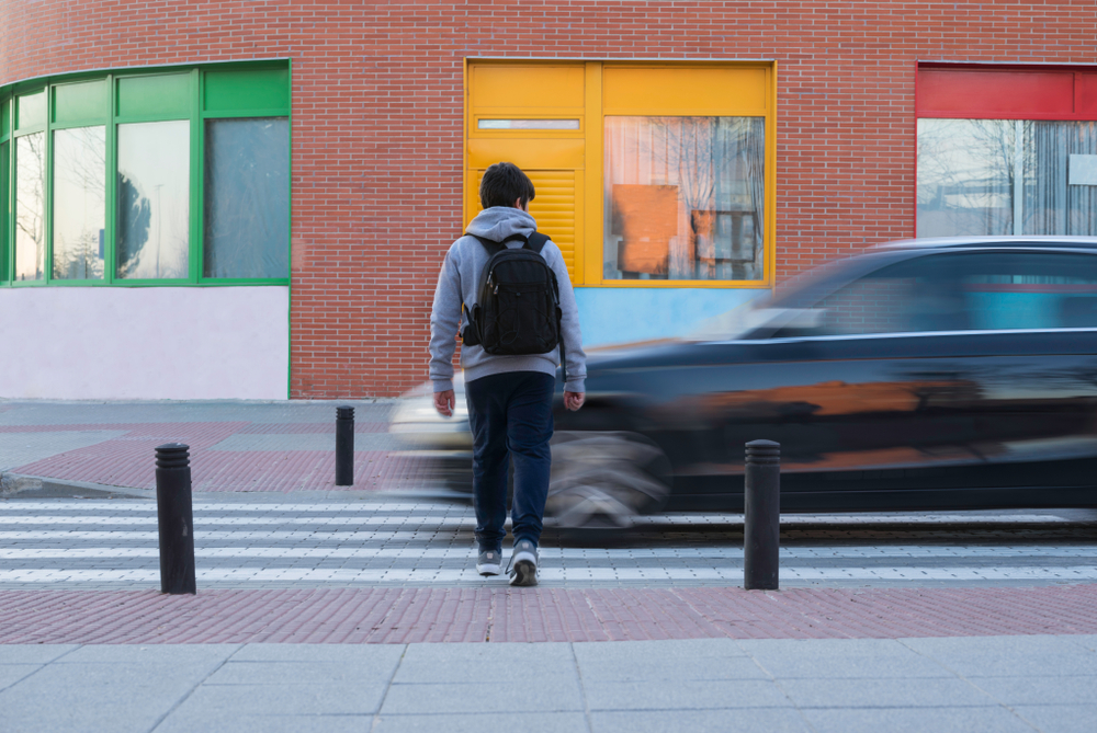 Pedestrian walking toward a crosswalk as a speeding car passes, showing common risk factors for pedestrian accidents.