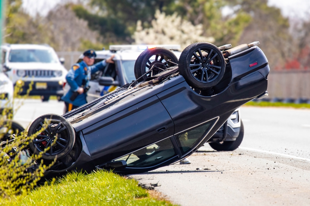 Rollover accident scene in Arlington, Texas Overturned black car on the roadside after a rollover accident, with police officers assisting at the scene in Arlington, Texas