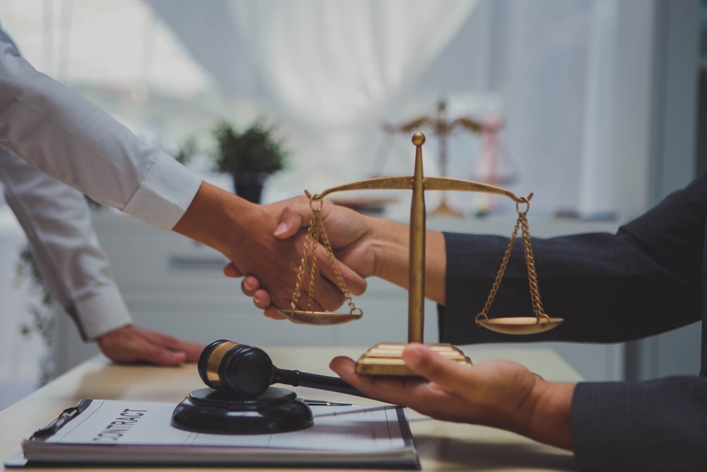Lawyer and client shaking hands at a desk with a gavel and scales of justice, representing legal help after a bicycle accident.
