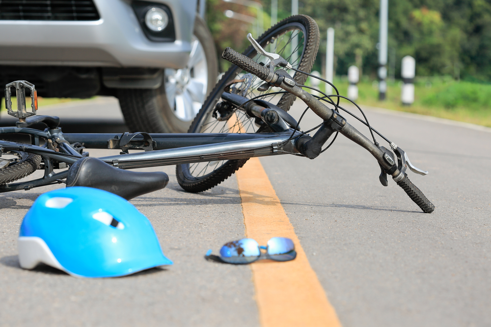Bicycle lying on the road next to a car with a helmet and sunglasses scattered nearby, representing a bike accident scene in Texas
