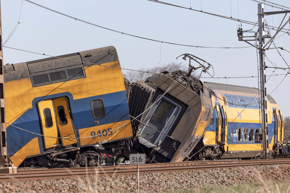 Yellow and blue passenger train derailed on railway tracks with visible damage to multiple cars.
