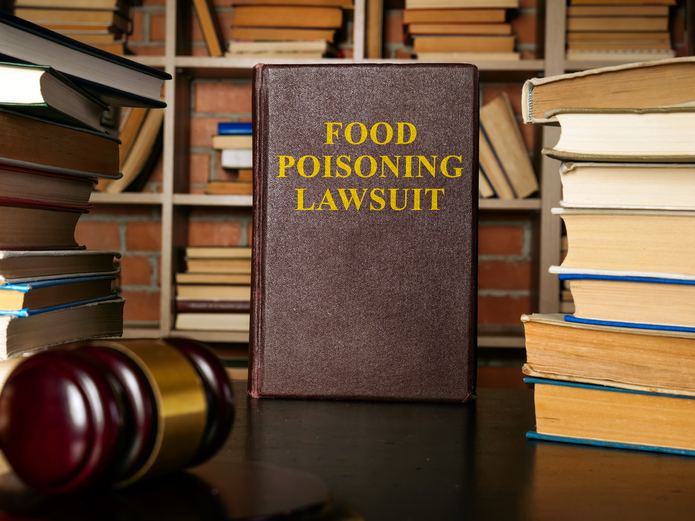 Law book labeled “Food Poisoning Lawsuit” next to a judge’s gavel in a legal office.