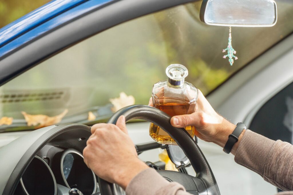 A driver holding a glass bottle while steering in Arlington, highlighting dangerous and common types of distractions while driving.