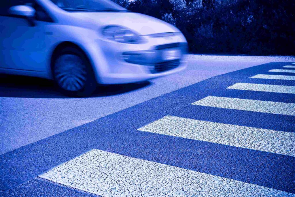 Speeding vehicle blurred while crossing a crosswalk at night, reflecting why speeding is a factor in 35% fatal accidents in Texas.