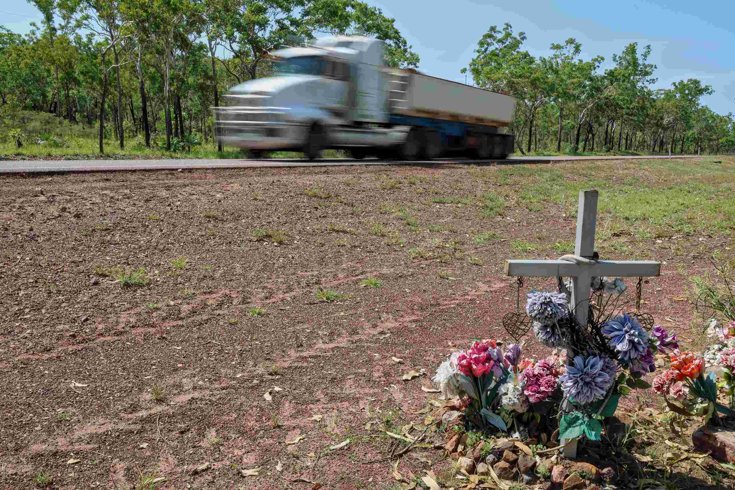 A roadside cross with flowers as a semi-truck blurs past, representing a fatal truck accident in Texas.