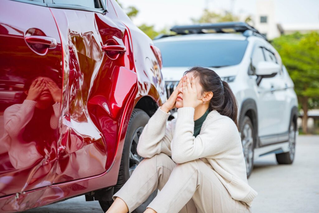 Driver sitting beside damaged car after getting into a car accident in a friend’s car in Texas while dealing with insurance and claim concerns