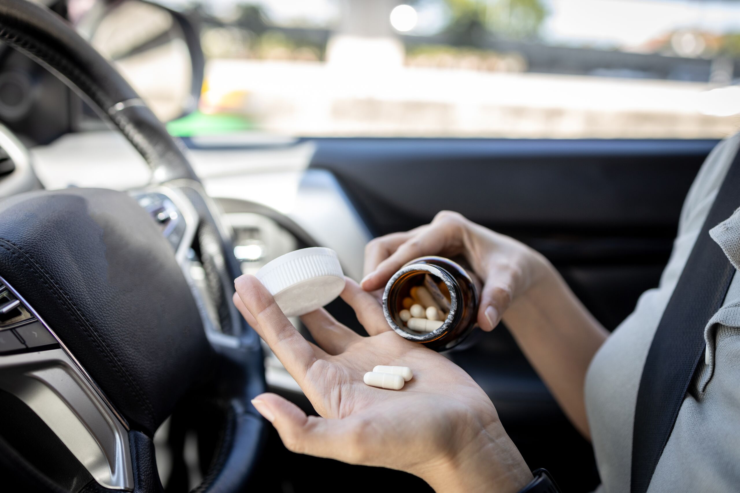 Driver holding prescription pills inside a vehicle while illustrating the dangers of drug-impaired driving accidents and impaired drivers in Texas