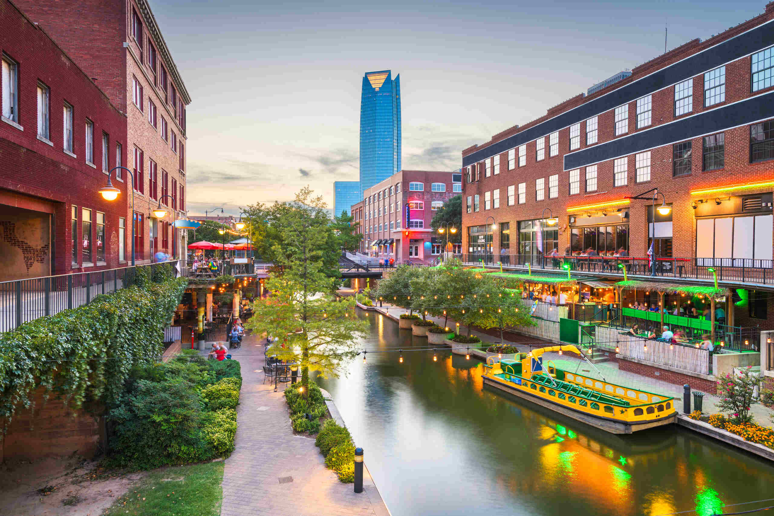 Evening view of the Bricktown Canal in Oklahoma City, lined with restaurants and a water taxi, providing local context for Oklahoma City Bicycle Accident Attorneys.