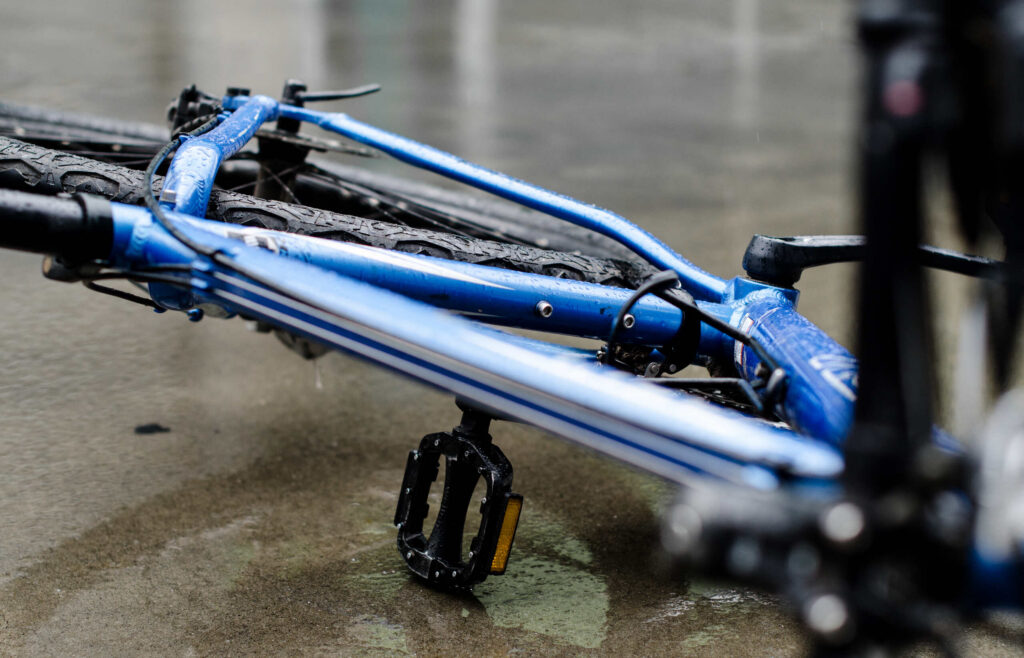 A blue bicycle lying flat on a wet, asphalt ground after a crash, illustrating case types handled by Oklahoma City Bicycle Accident Attorneys.