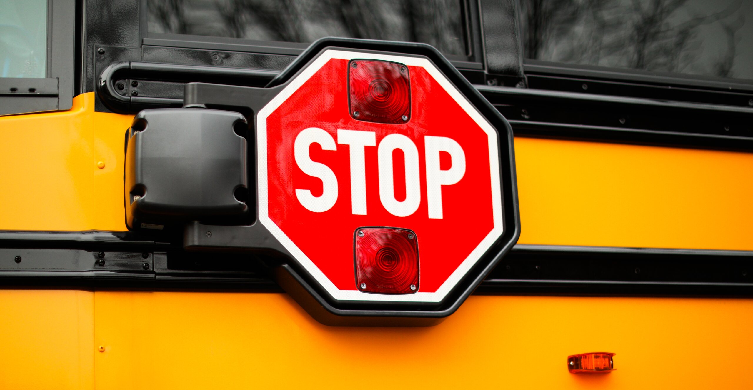 Close-up of a red stop sign arm with flashing lights mounted on the side of a yellow school bus, illustrating cases handled by Oklahoma City Bus Accident Attorneys.