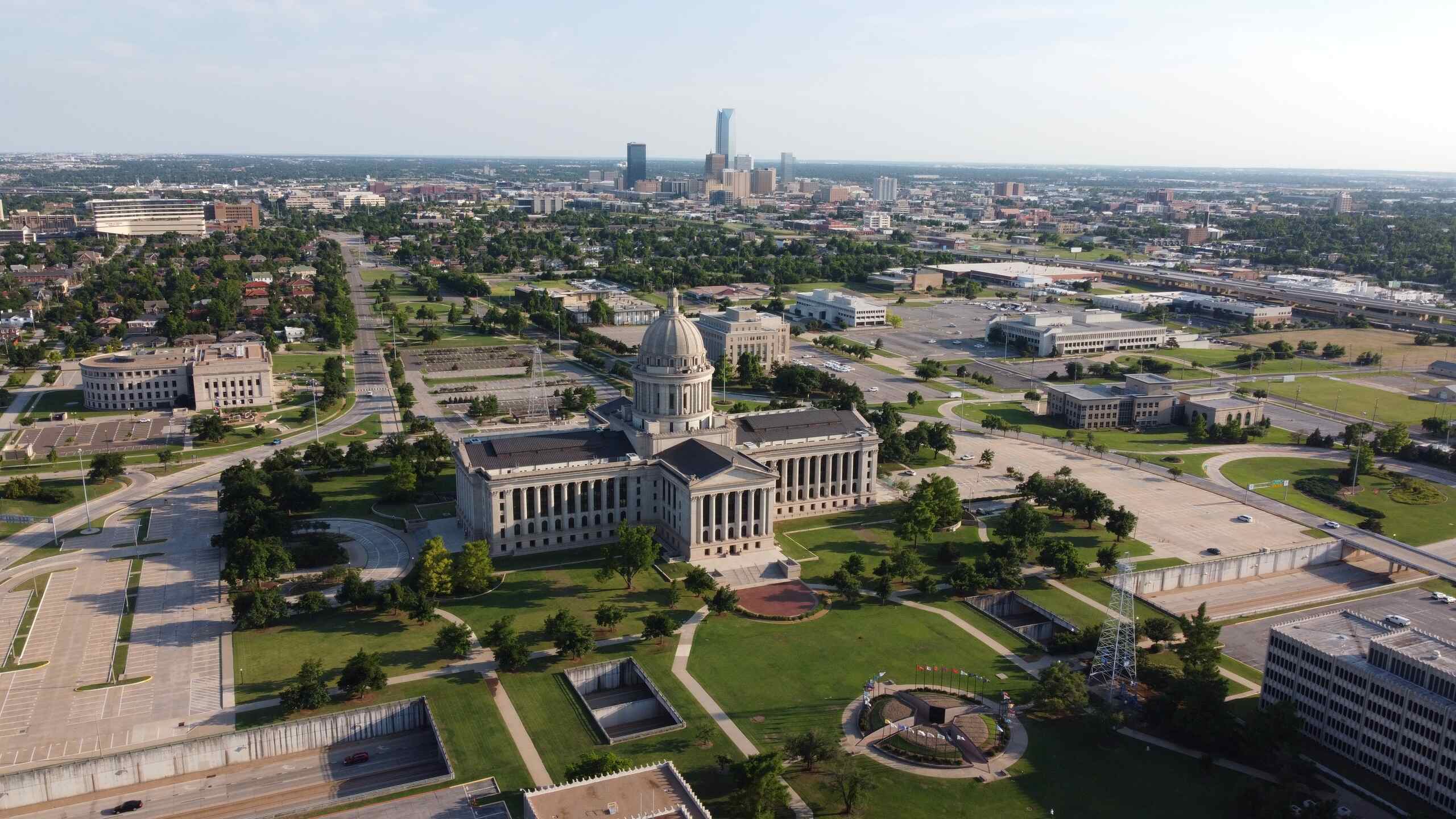 Wide aerial view of the Oklahoma State Capitol building and surrounding grounds with the downtown city skyline in the background, providing local context for Oklahoma City Car Accident Attorneys.