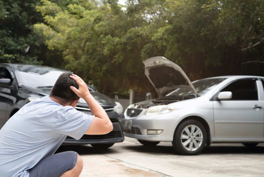 A stressed driver with his hands on his head looks at a two-car fender bender involving a silver sedan with its hood open, illustrating case types handled by Oklahoma City Car Accident Attorneys.