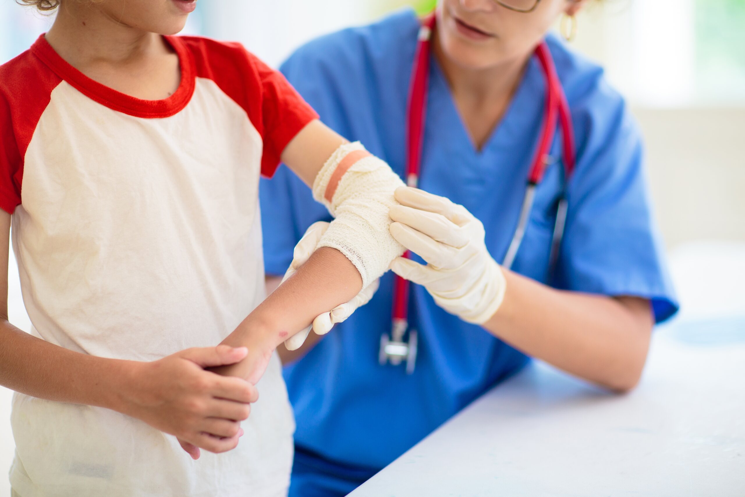 A medical professional in blue scrubs wraps a bandage around a child