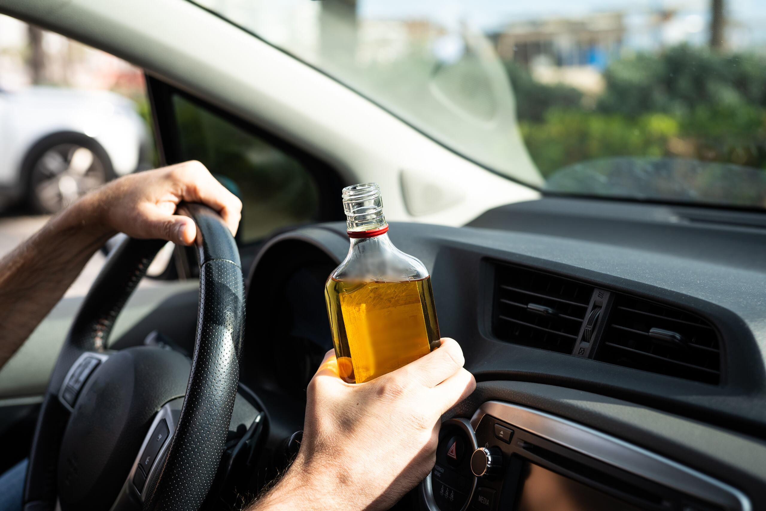 Close-up of a driver holding an open liquor bottle at the steering wheel of a car, illustrating cases managed by Oklahoma City Drunk Driving Accident Attorneys.
