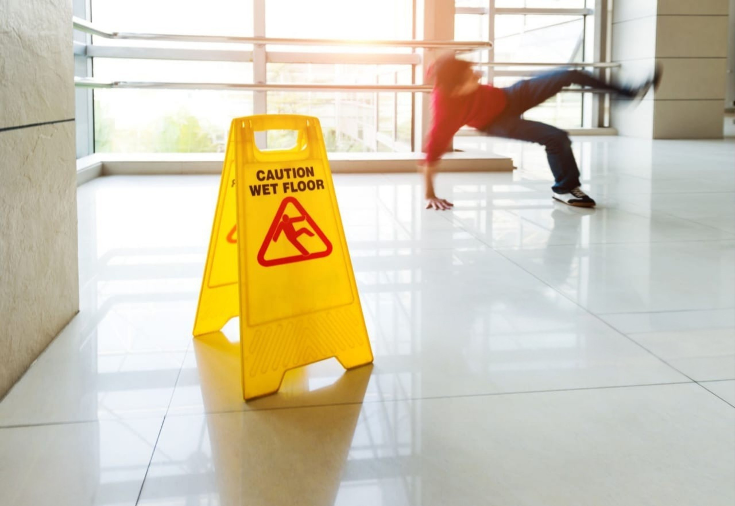 Person slipping on a wet floor near a caution sign, handled by Oklahoma City premises liability attorneys.