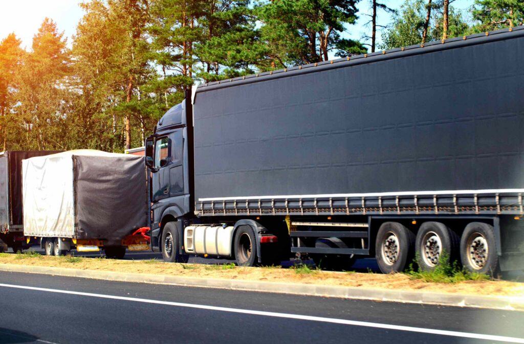 A large black commercial semi-truck with a flatbed trailer parked along the shoulder of a highway next to a treeline, illustrating cases handled by Oklahoma City Truck Accident Attorneys.