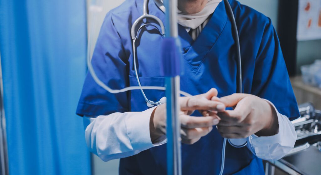 Close-up of a healthcare professional in blue scrubs with a stethoscope adjusting an IV line, representing medical malpractice or severe injury cases handled by Oklahoma City Personal Injury Attorneys.