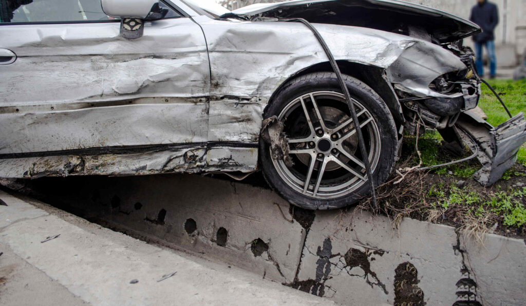 A damaged car stuck over a concrete ledge raises questions about who is liable if a road hazard causes an OKC car accident.