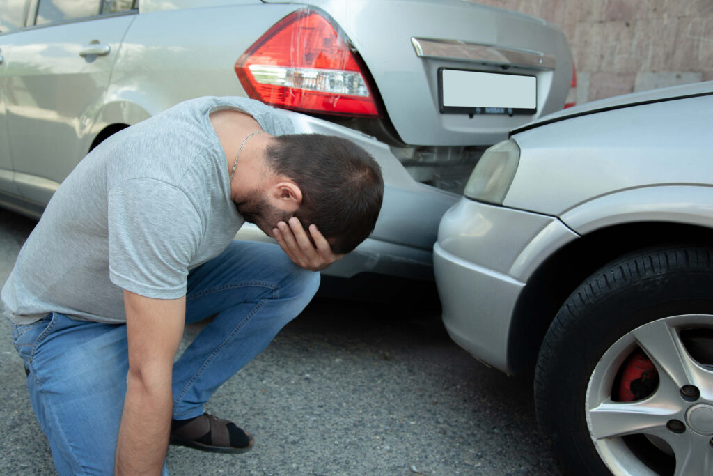 A stressed driver crouching near his crashed vehicle wonders who pays for my injuries if driver is uninsured in Oklahoma City.