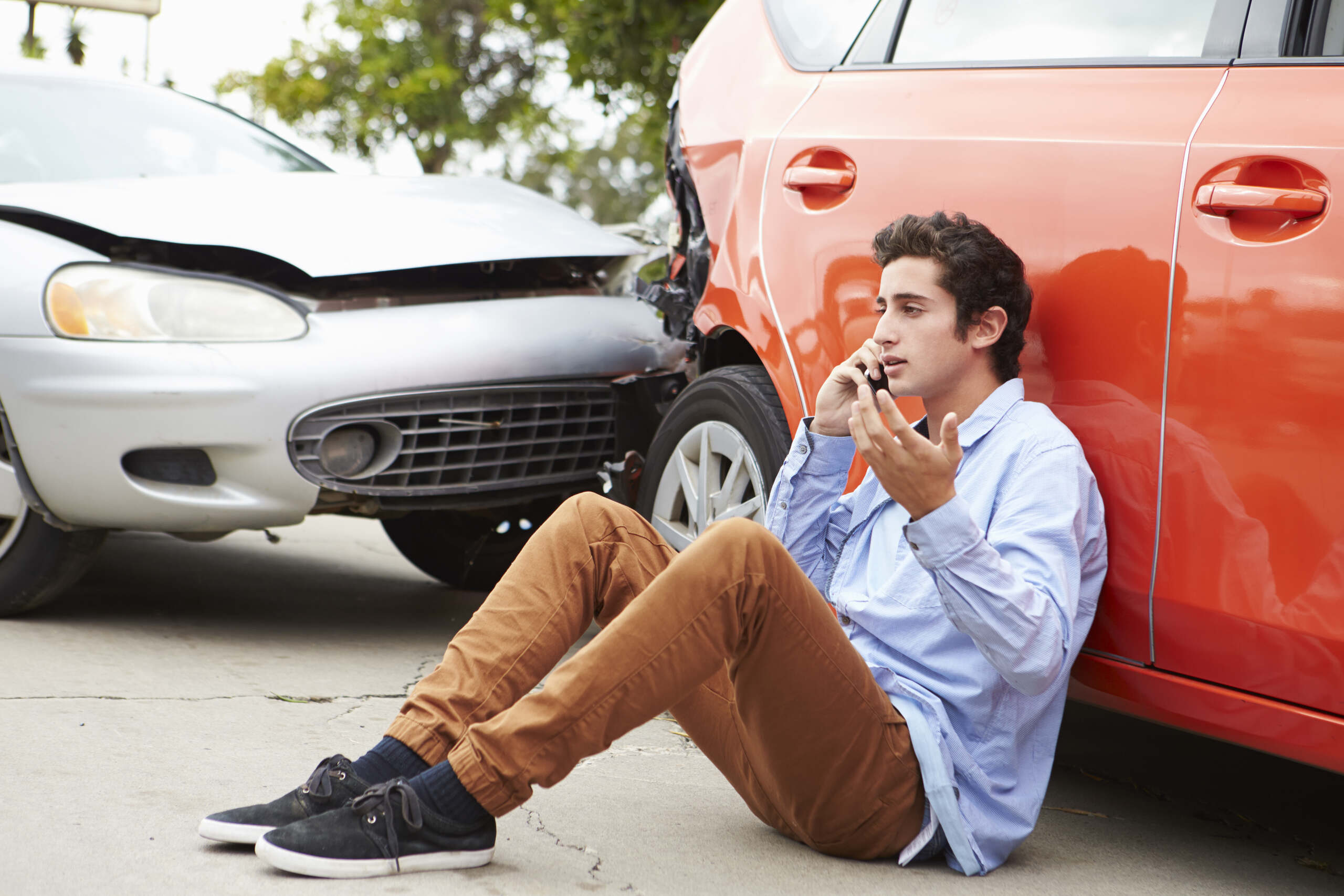A driver sitting on the ground making a phone call next to his crashed car wonders who pays for rear end collision in Oklahoma City.