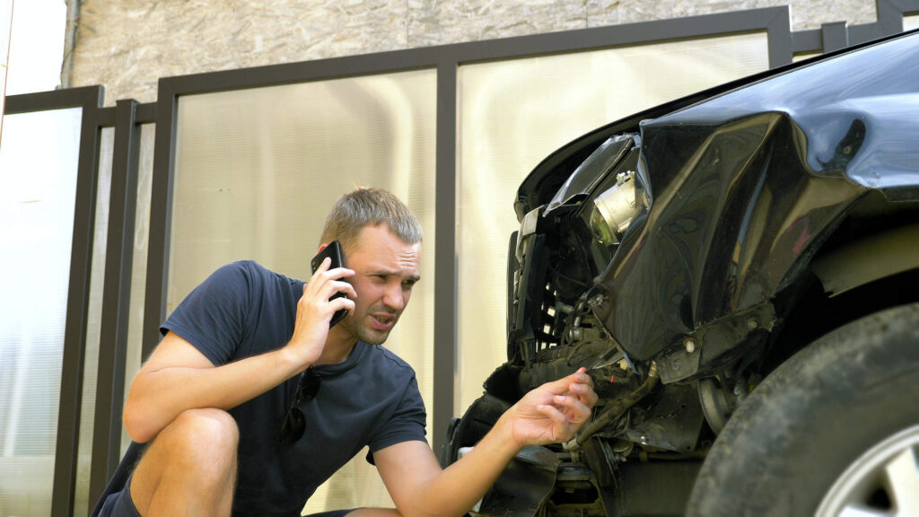 A worried driver calling for legal help near his wrecked car explains why do I need to hire an OKC hit and run accident attorney OKC crash.